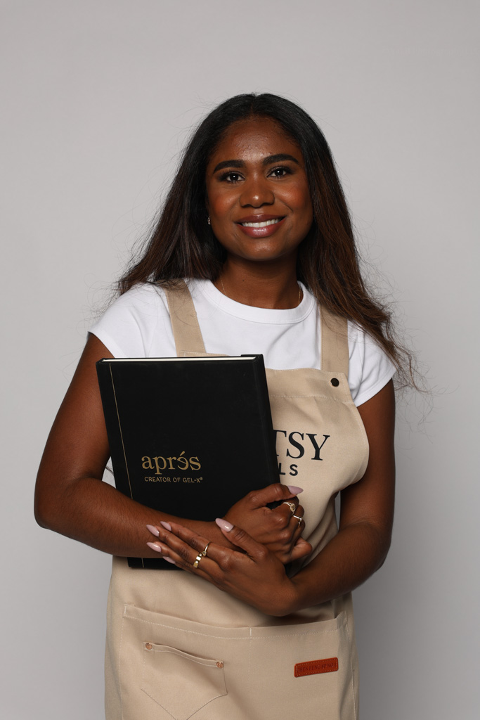 Natalia Granja holding an Aprés folder in her Artsy Nails apron